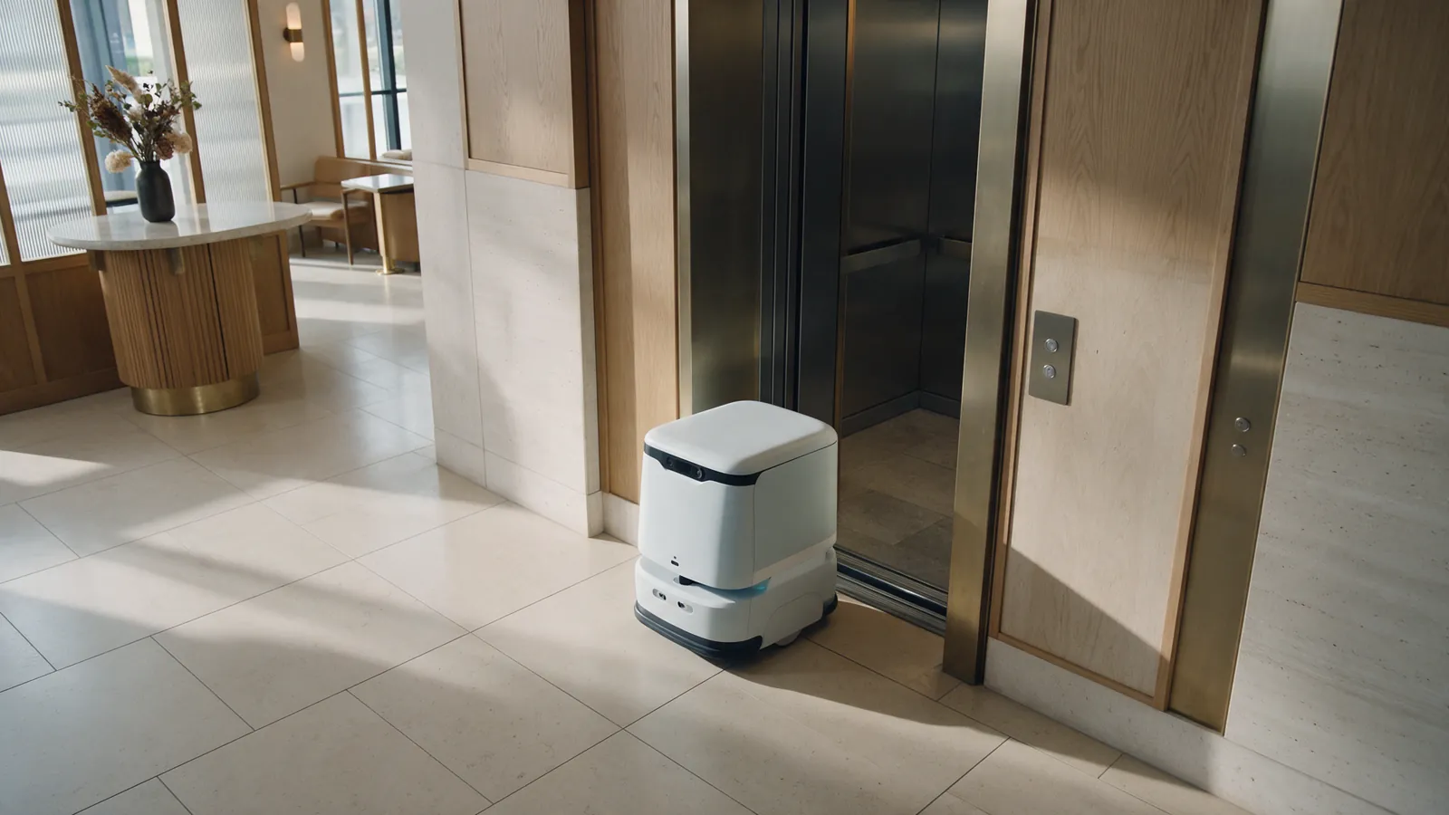 Illustrative delivery robot paused near an elevator threshold in a hotel lobby.
