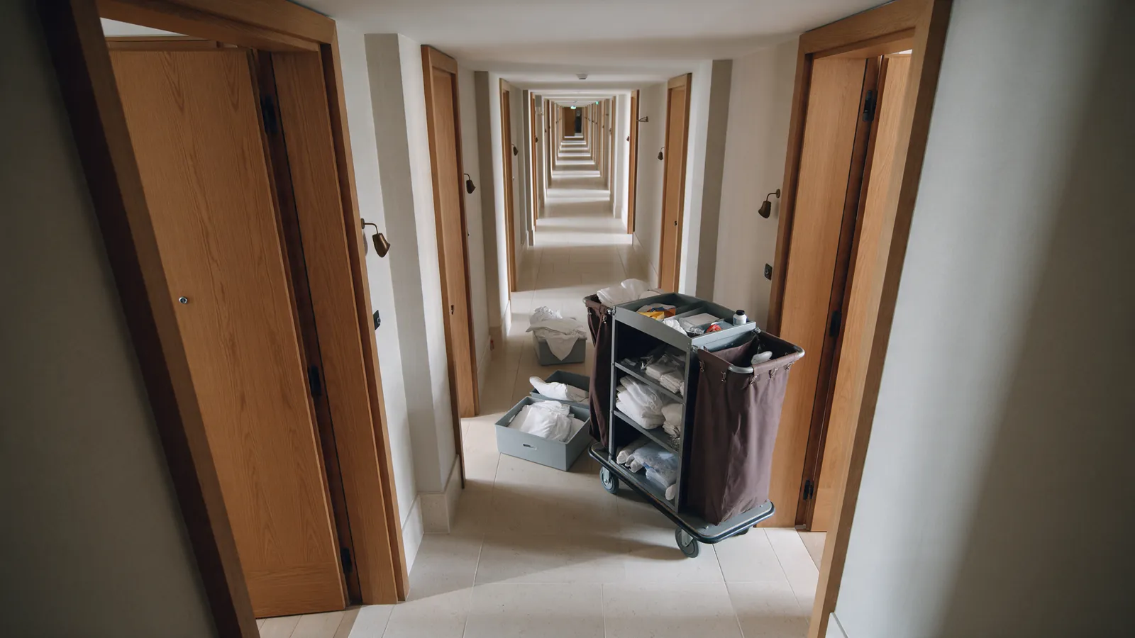 Illustrative hotel corridor narrowed by a housekeeping trolley and cartons.