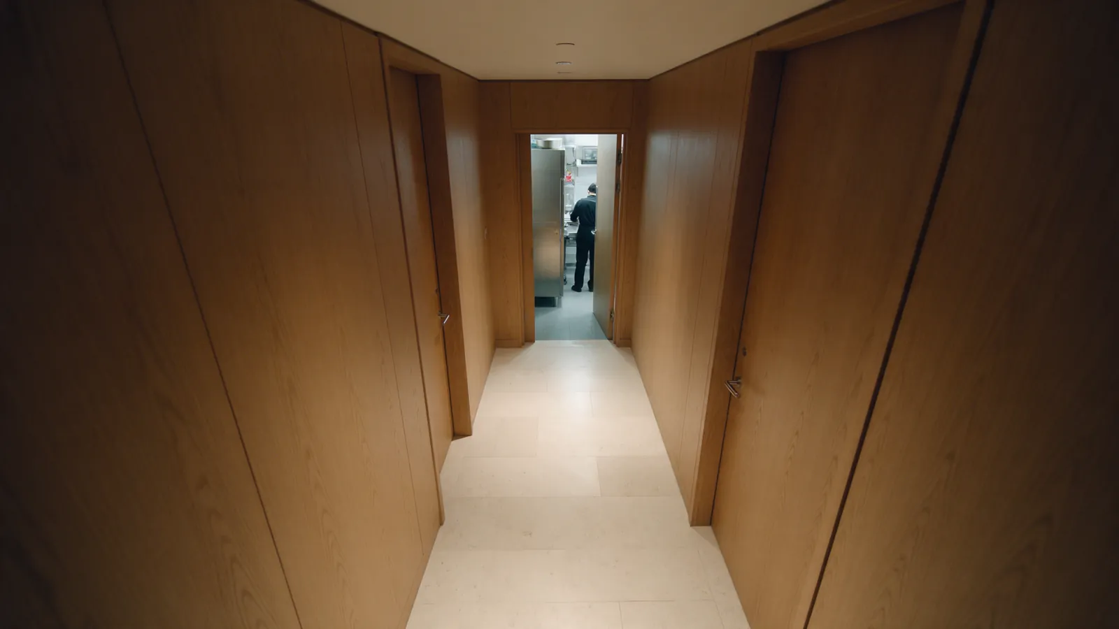 Illustrative hotel staff corridor with a distant person near a restricted doorway.